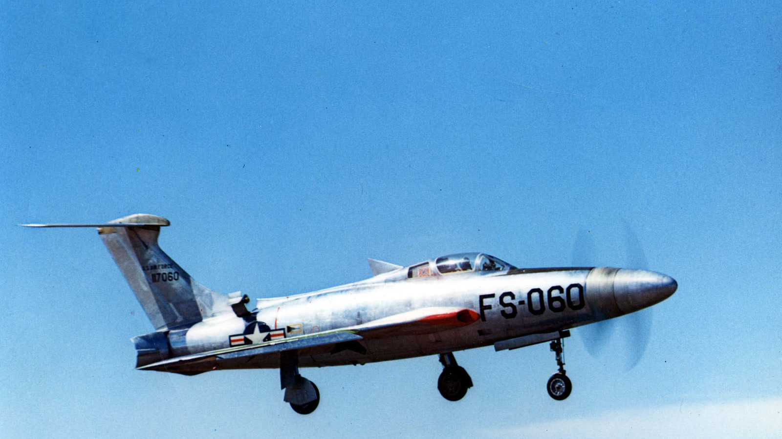 Republic XF-84H Thunderscreech serial 51-17060 (buzz number FS-060) in flight with landing gear down, silver T-tail fighter and blurred nose propeller against blue sky